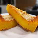 Fatias de queijada de laranja cremosa com cobertura de coco crocante servidas num prato branco.